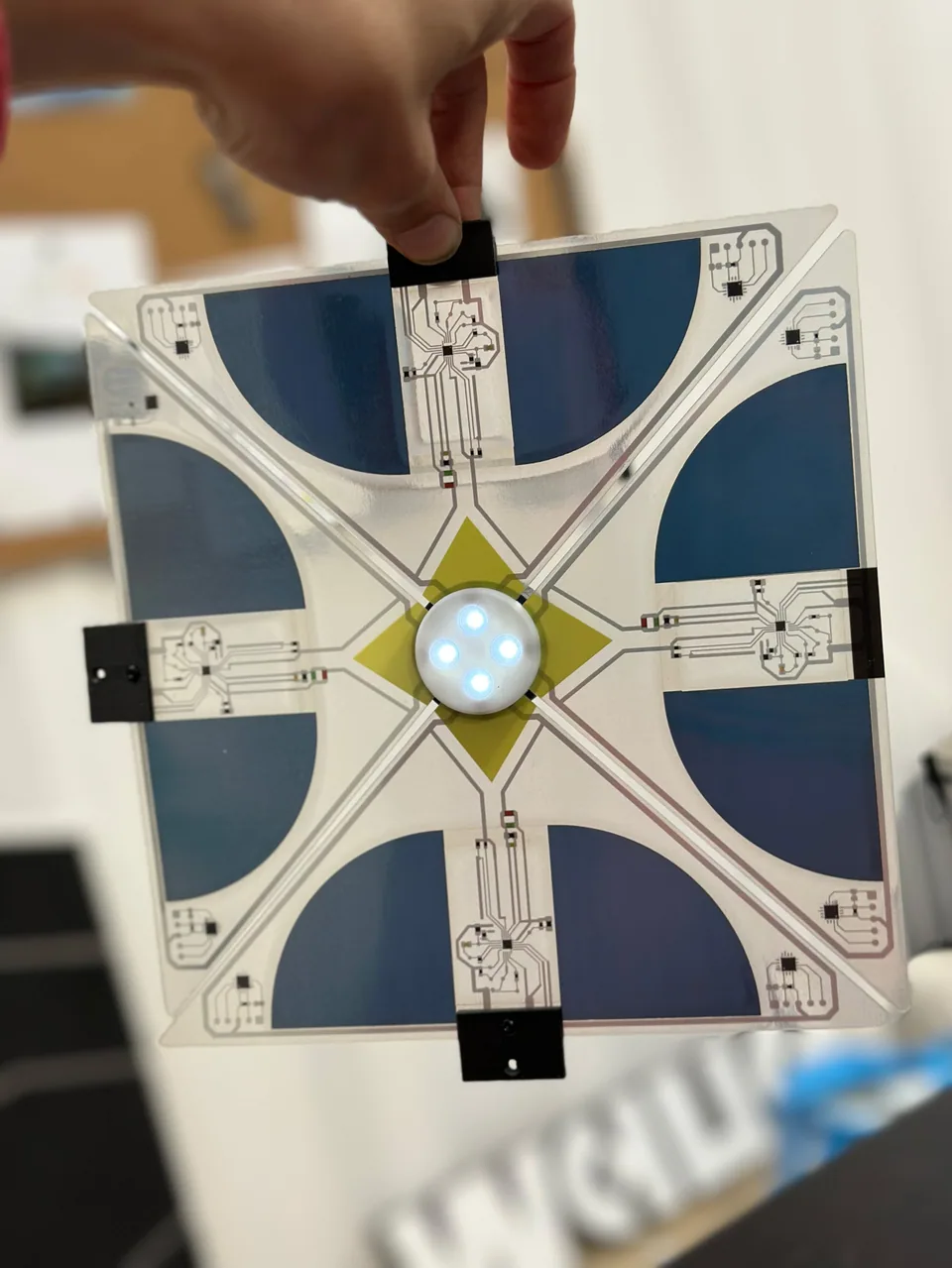 Hand holding a translucent Between Lights prototype with printed circuits, flexible solar cells and four illuminated LEDs