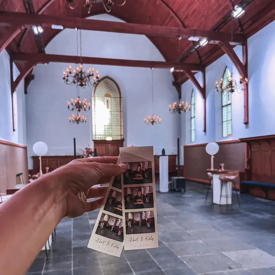Printed photobooth strips held up inside a wedding venue with chandeliers and stained-glass windows